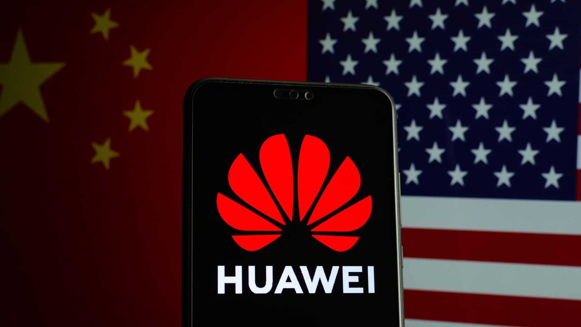 Logo da Huawei exibido em smartphone e ao fundo bandeiras da China e Estados Unidos