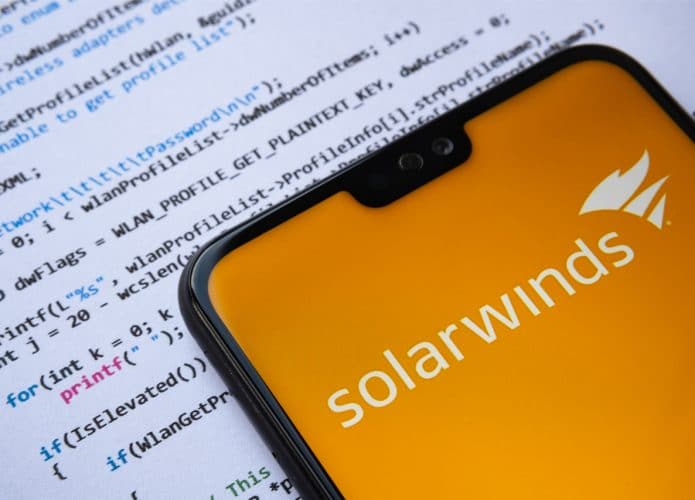Imagem mostra um smartphone com a logomarca da SolarWinds, em cima de folhas de papel com linhas de código escritas em várias cores