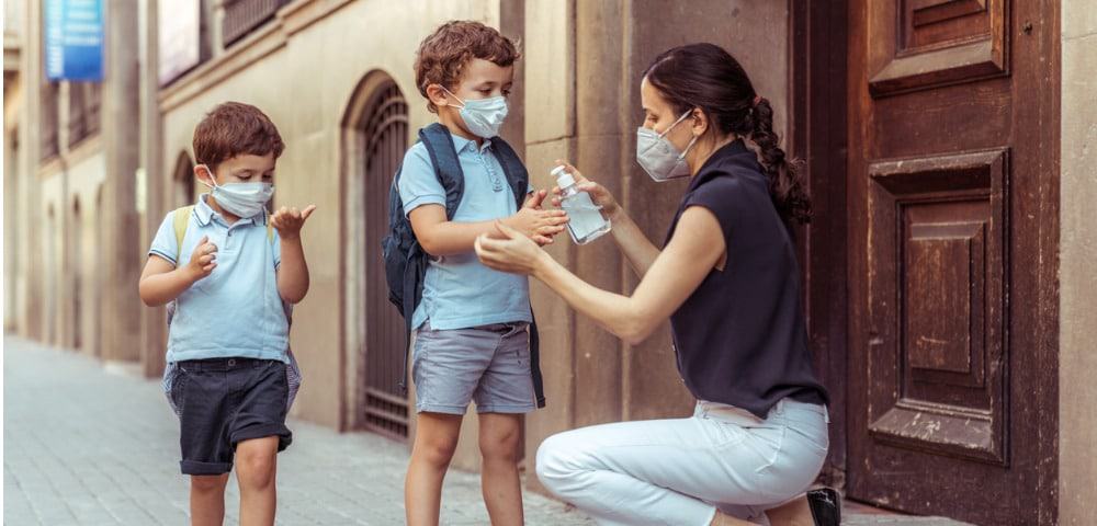 teacher-using-hand-sanitizer-with-kids-going-back-to-school-picture-id1226271017