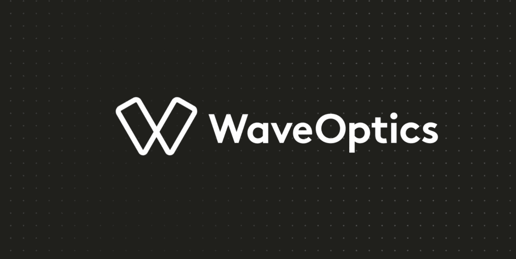 Imagem possui fundo preto com um padrão de pequenas bolinhas; à frente está o logotipo da marca WaveOptics, especializada em tecnologia para realidade aumentada