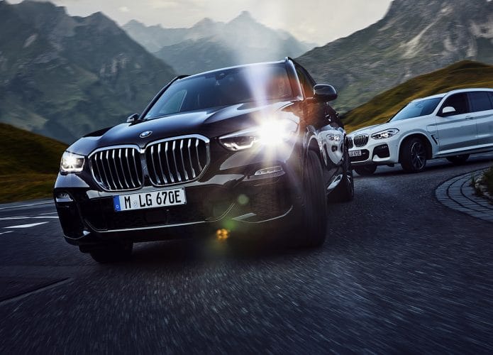 Imagem exibe BMW X3 preto em estrada com paisagem montanhosa.