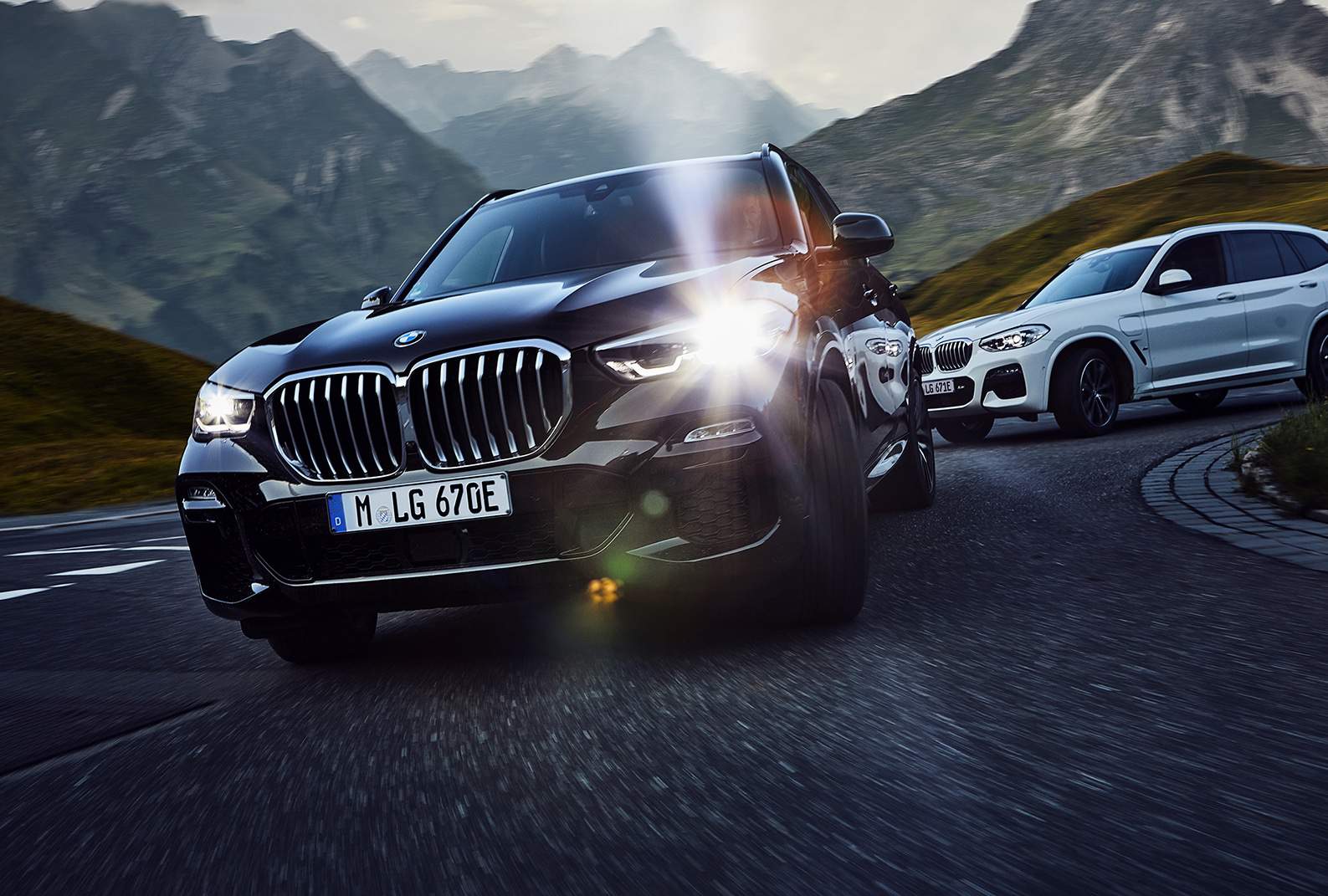 Imagem exibe BMW X3 preto em estrada com paisagem montanhosa.