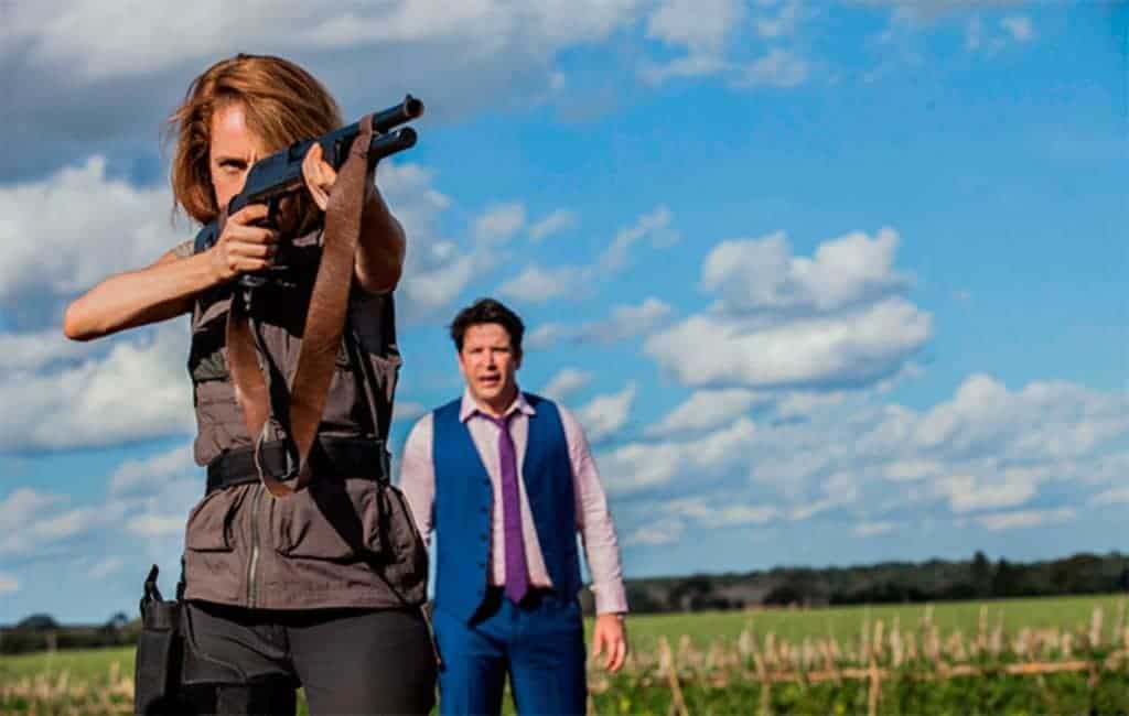 Camila Morgado segura espingarda em cena do filme Divórcio, com personagem de Murilo Benício em segundo plano, observando a situação.