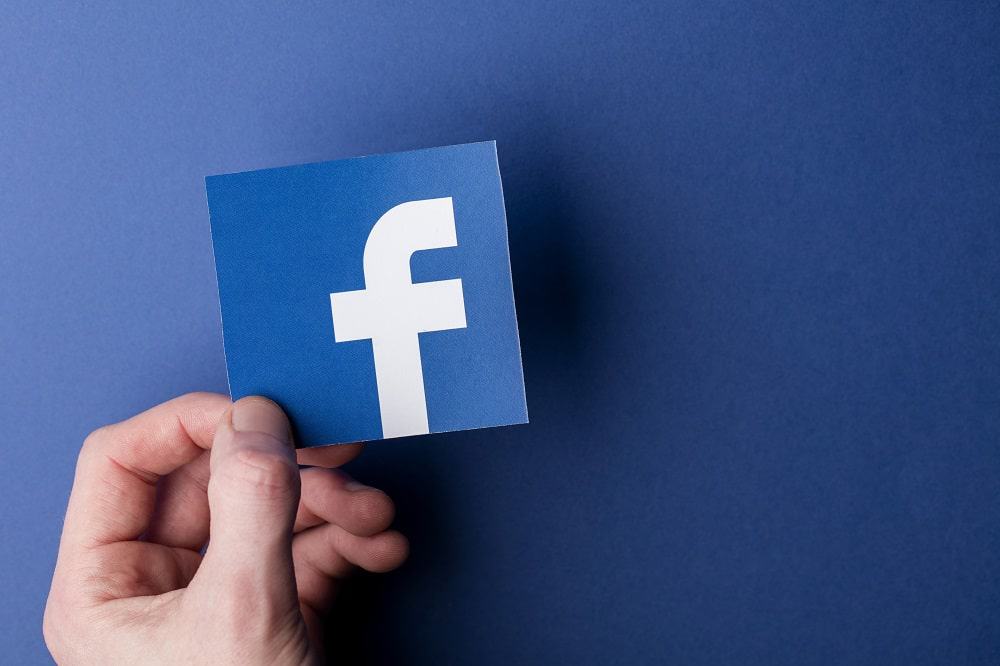 Imagem mostra uma mão segurando o logotipo do Facebook em um fundo azul