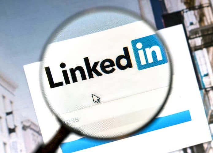 Imagem mostra o logotipo do LinkedIn aberto em uma página web; uma lupa está posicionada em cima do logotipo, aumentando seu tamanho