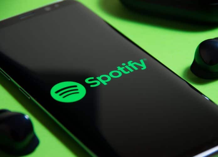 Logo do Spotify aparece na tela de um smartphone colocado em cima de um fundo verde limão