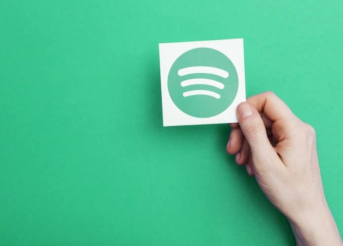 Imagem de fundo verde mostra uma mão segurando um cartão com o logotipo do Spotify
