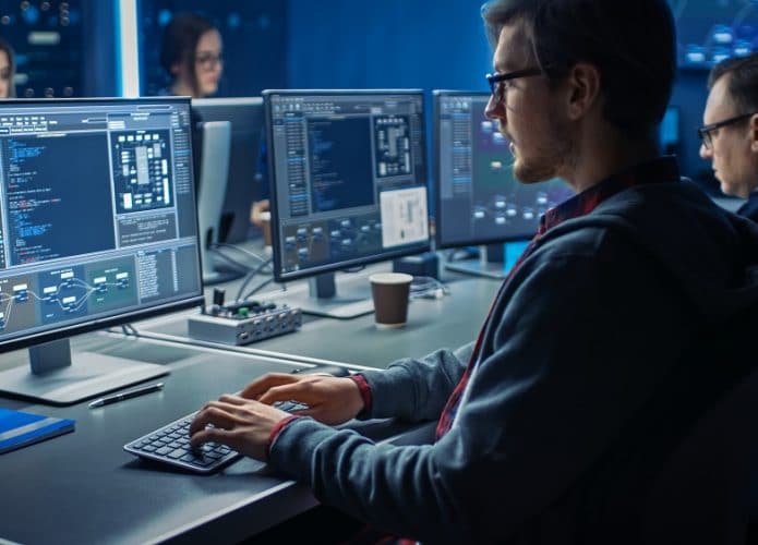 Imagem mostra homem sentado em uma mesa, digitando em um teclado de computador olhando para a tela do PC
