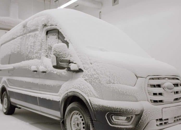 Imagem exibe Ford E-Transit coberto de neve em sala de testes.