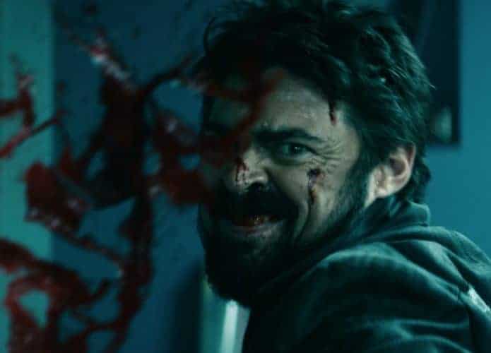 O ator Karl Urban aparece caracterizado como Billy Butcher enquanto sorri com o rosto ensanguentado