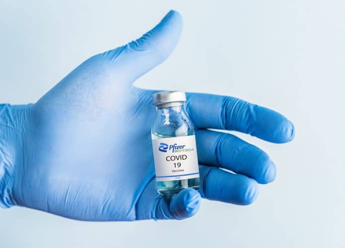 Mão de luva azul segurando um frasco de vidro da vacina da Pfizer contra a Covid-19
