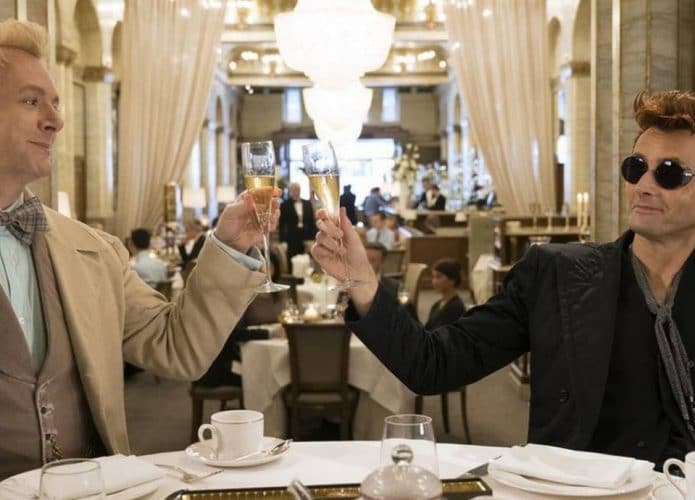 Em cena da primeira temporada, Michael Sheen (Aziraphale) e David Tennant (Crowley) aparecem brindando em uma mesa.