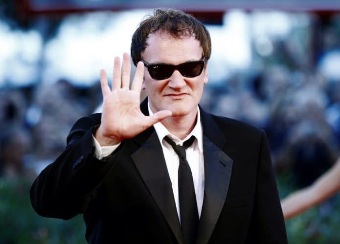 Quentin Tarantino de fraque e óculos escuro exibindo a palma da mão.
