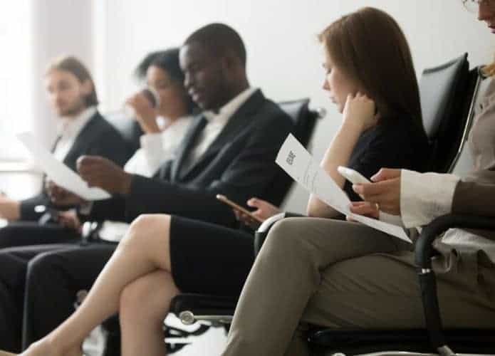 Cinco pessoas estão sentadas, uma ao lado das outras, esperando para serem chamadas para a entrevista de emprego.