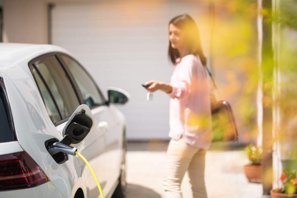 Mulher em pé ao lado de um carro elétrico sendo carregado 