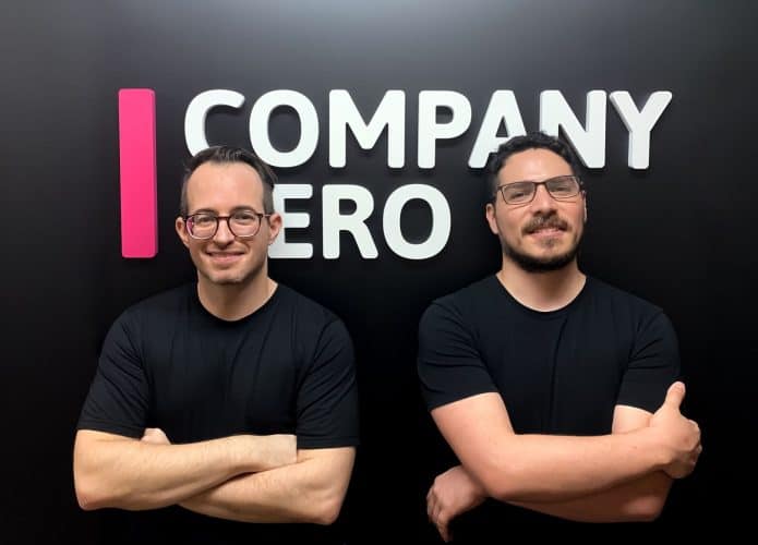 Na imagem, os cofundadores da Company Hero, Miklos Grof e Diego Izquierdo; ao fundo, em uma parede preta, está o logo da empresa em letra caixa