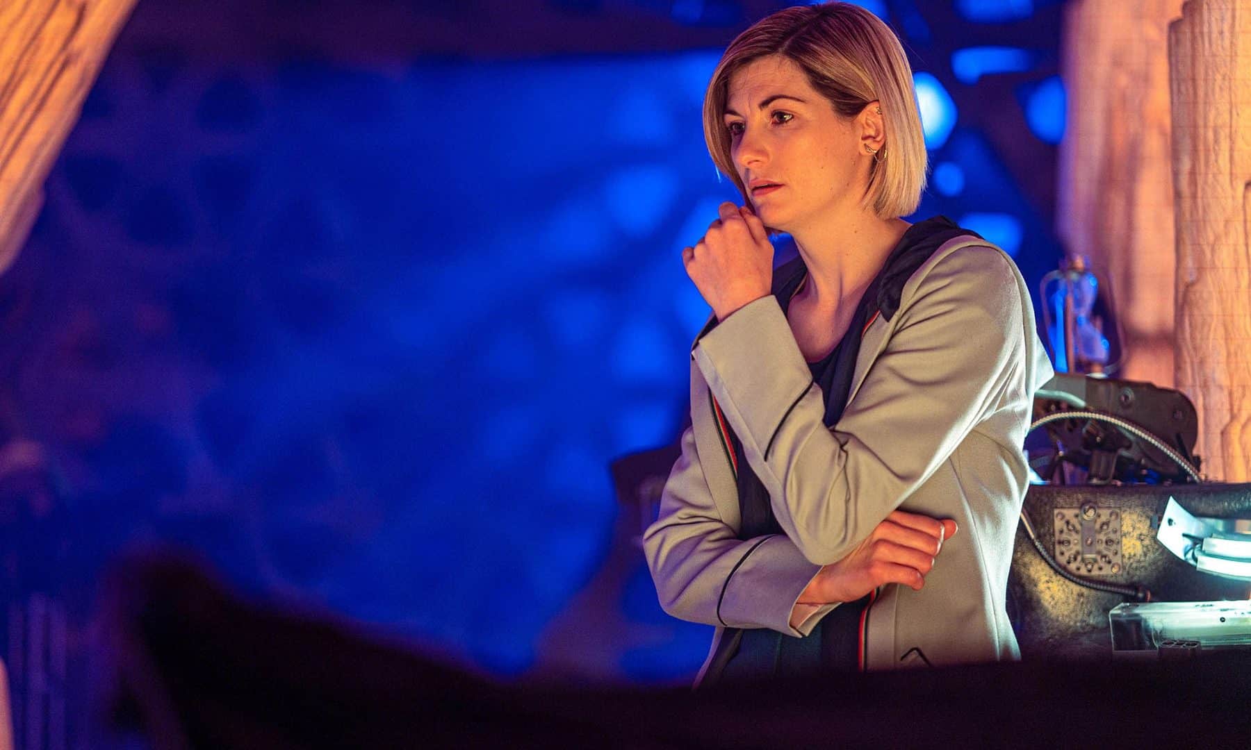 A atriz Jodie Whittaker caracterizada como Doctor aparece em foto com a mão no queijo e olhar pensativo.