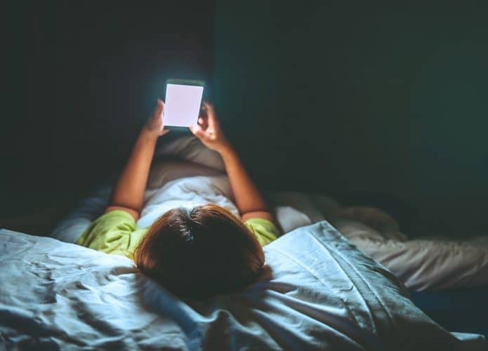 mulher deitada no escuro com celular com luz forte