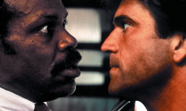 Danny Glover e Mel Gibson se encarando em cena do primeiro filme. 