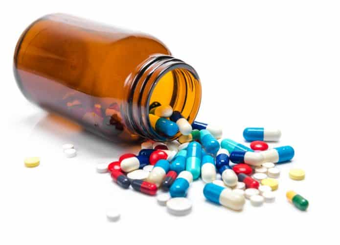 Imagem mostra várias pílulas medicinais despejadas de um frasco de vidro