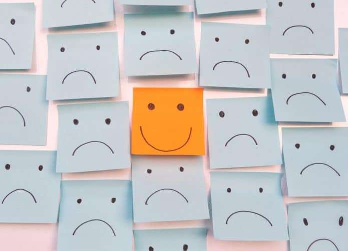 Post-its azuis com desenhos de rostos tristes ao redor de um post-it laranja com o desenho de um rosto feliz