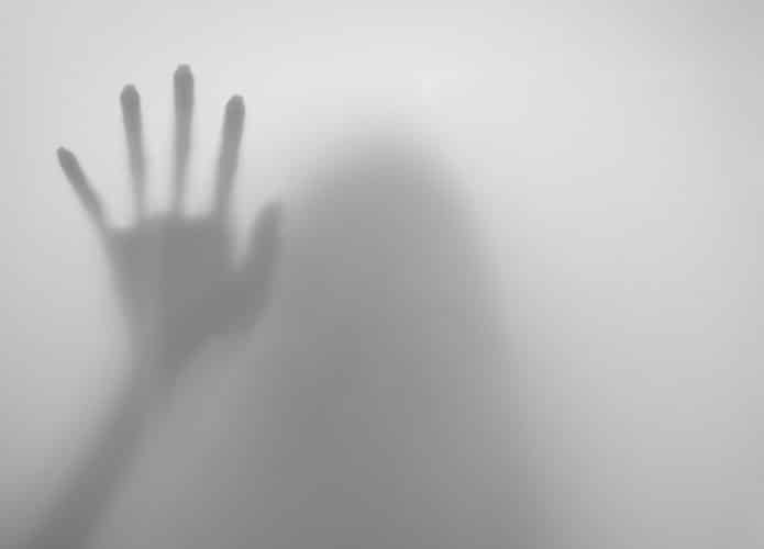 mulher atrás de película branca esticando a mão parecendo um fantasma