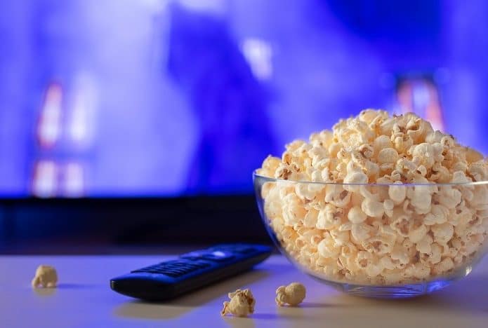 pipoca e controle em cima de uma mesa com uma TV ao fundo