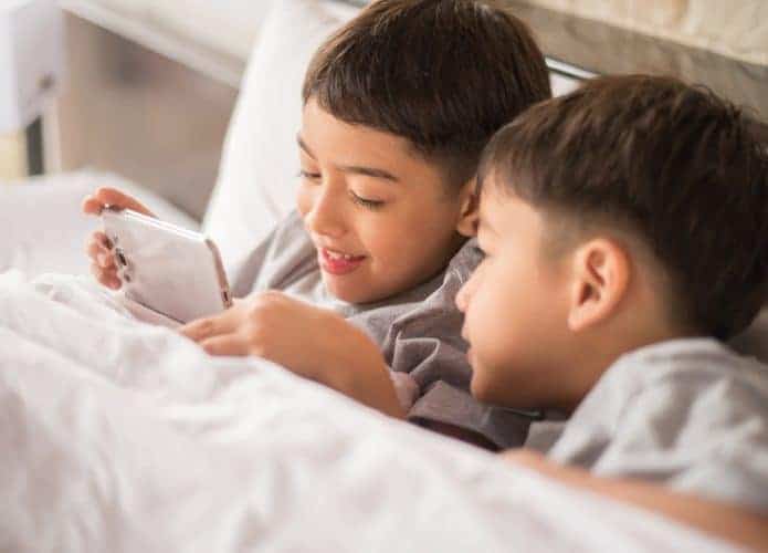 Duas crianças assistem a vídeo no celular na cama