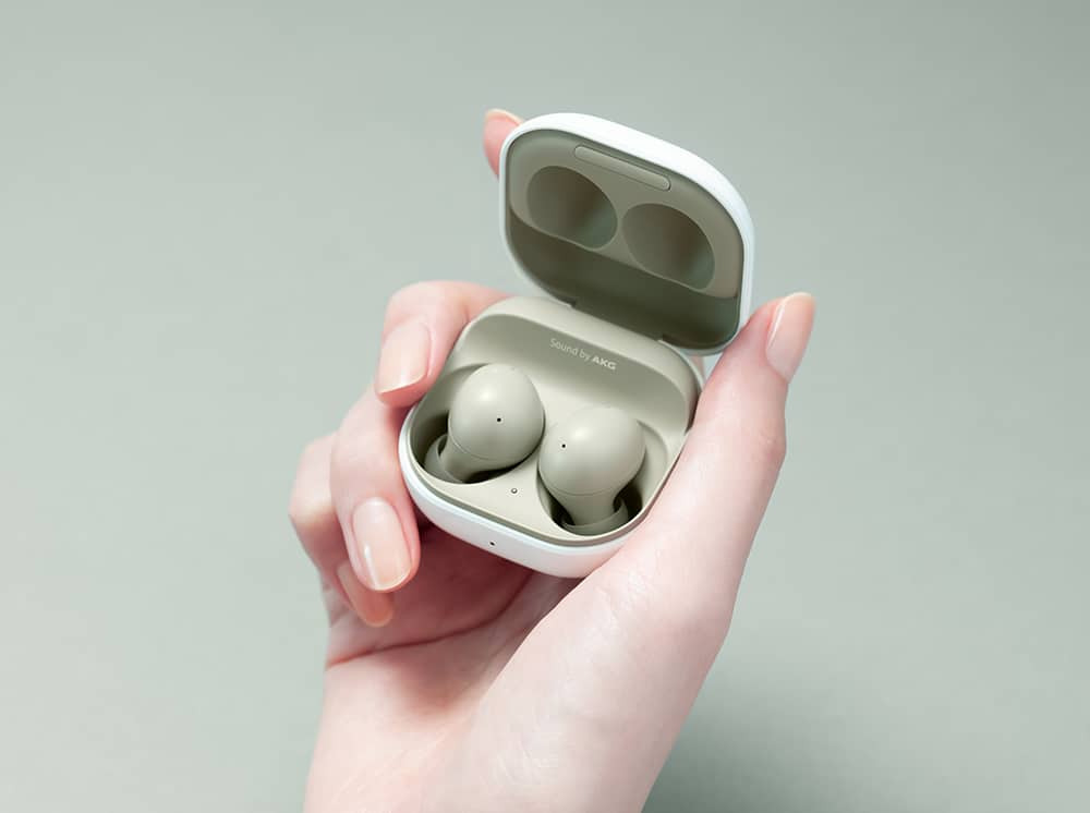 Imagem mostra uma mão de mulher segurando um case aberto onde, dentro, podemos ver os fones Galaxy Buds 2