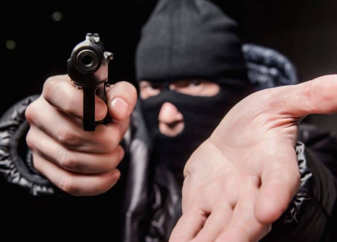 criminoso de balaclava apontando arma e estendendo a mao