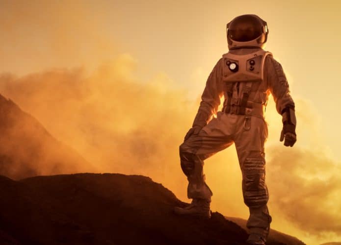 Imagem conceitual mostra um astronauta caminhando por região montanhosa de Marte