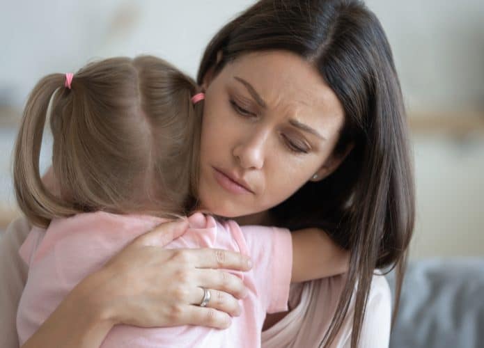 Imagem mostra uma mãe preocupada abraçando a sua filha. A mãe tem cabelos longos e pretos, enquanto a menina tem o cabelo amarrado em duas partes