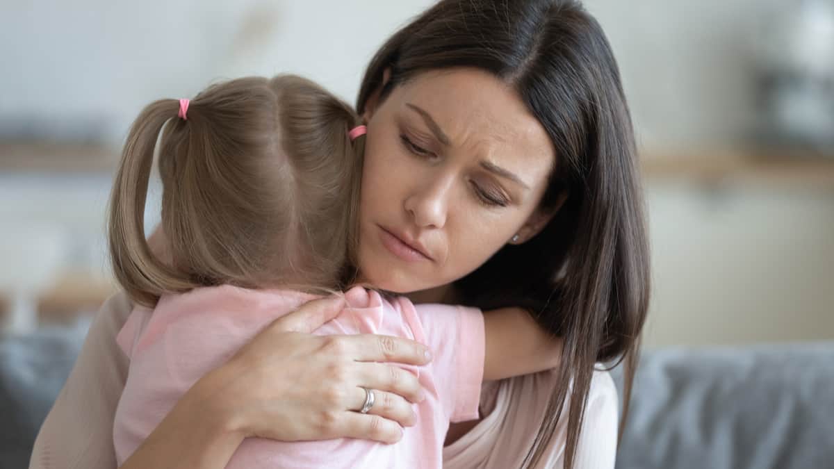 Imagem mostra uma mãe preocupada abraçando a sua filha. A mãe tem cabelos longos e pretos, enquanto a menina tem o cabelo amarrado em duas partes