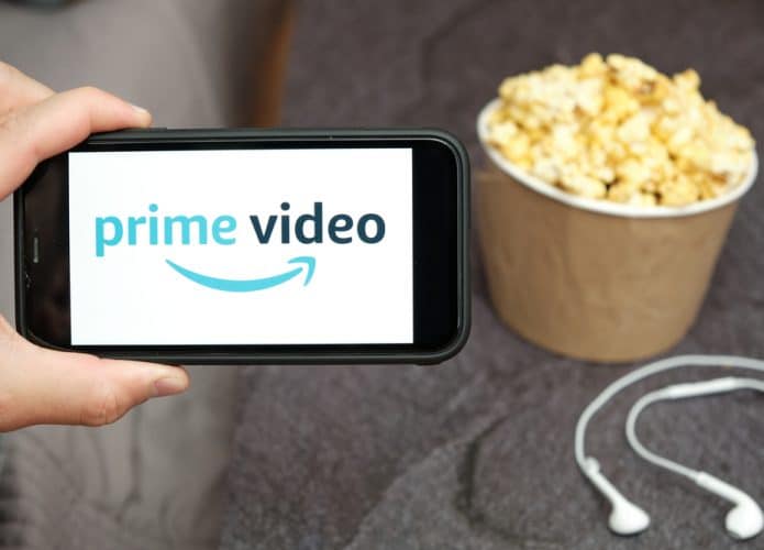 Homem segurando um smartphone com o logotipo do Amazon Prime Video e uma caixa de pipoca ao lado