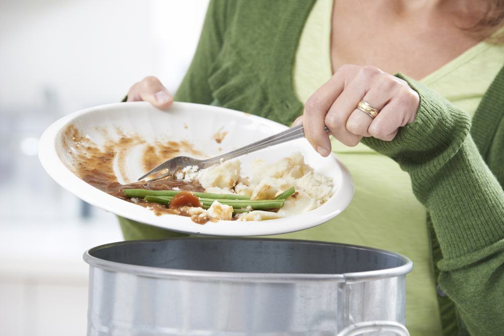 Mulher raspando sobras de alimentos em uma lixeira
