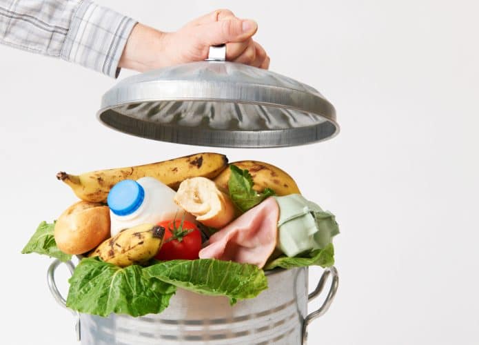 Mão coloca uma tampa na lata de lixo cheia de resíduos de alimentos