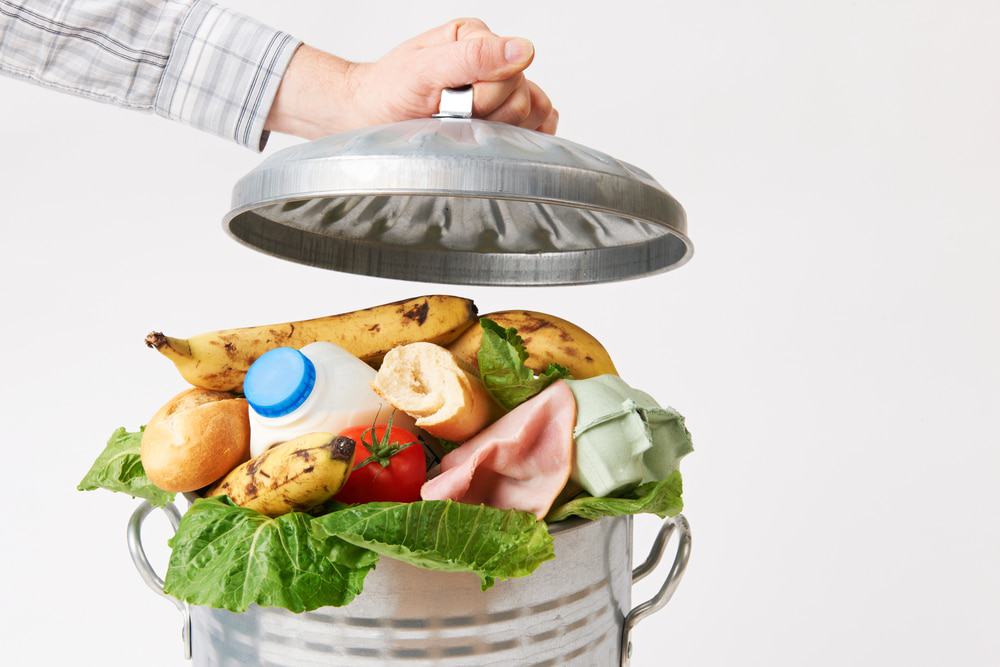 Mão coloca uma tampa na lata de lixo cheia de resíduos de alimentos