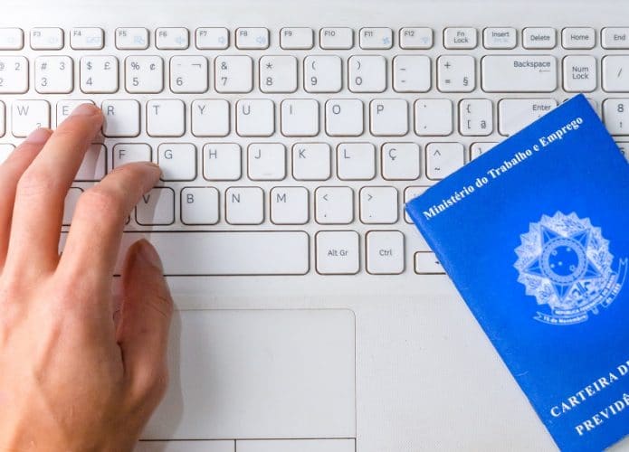 mão em cima do teclado com carteira de trabalho ao lado