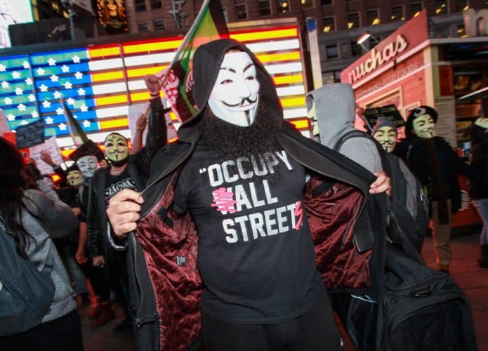 manifestante com máscara usando camiseta escrito occupy all streets em protesto nos estados unidos junto a diversas pessoas mascaradas