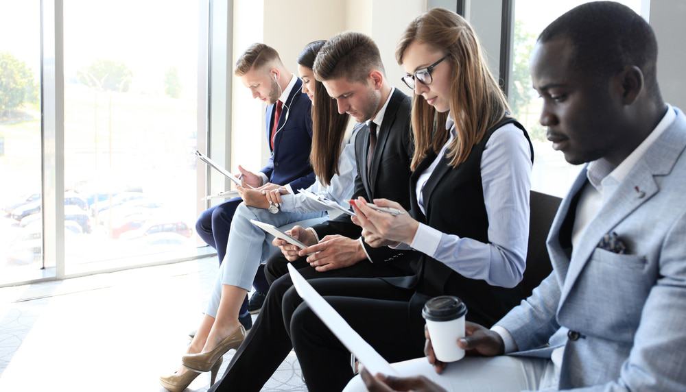Imagem mostra candidatos à entrevista de emprego esperando sentados, um ao lado dos outros