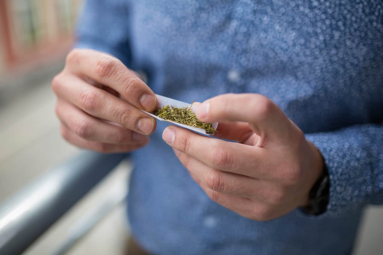 Homem enrolando um baseado de maconha