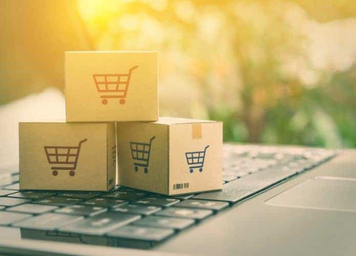 Conceito de comércio eletrônico com caixas e um carrinho de compras em um teclado de laptop. Imagem ilustra clientes encomendando produtos de sites de varejistas através da internet.