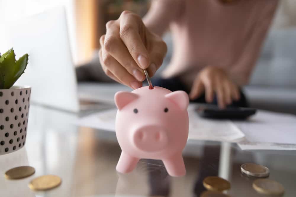 Jovem colocando moedas no cofrinho. Mulher economizando para pagamentos domésticos, contas, calculando orçamentos familiares mensais, fazendo investimentos ou estratégia para poupança pessoal