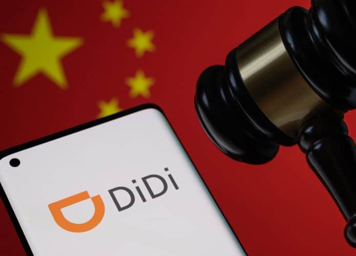 Logotipo da Didi Chuxing Technology exibido na tela de um smartphone com martelo e bandeira da China ao fundo, ilustrando o conceito de regulamentação governamental