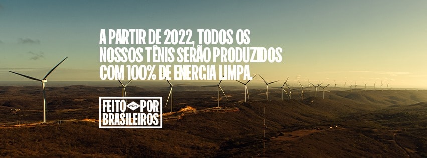 Imagem mostra ao fundo gerador de energia eólica. Pode se ler a frase: "a partir de 2022, todos os nossos tênis serão produzidos com 100% energia limpa", divulgação da Vulcabras para a marca Olympikus