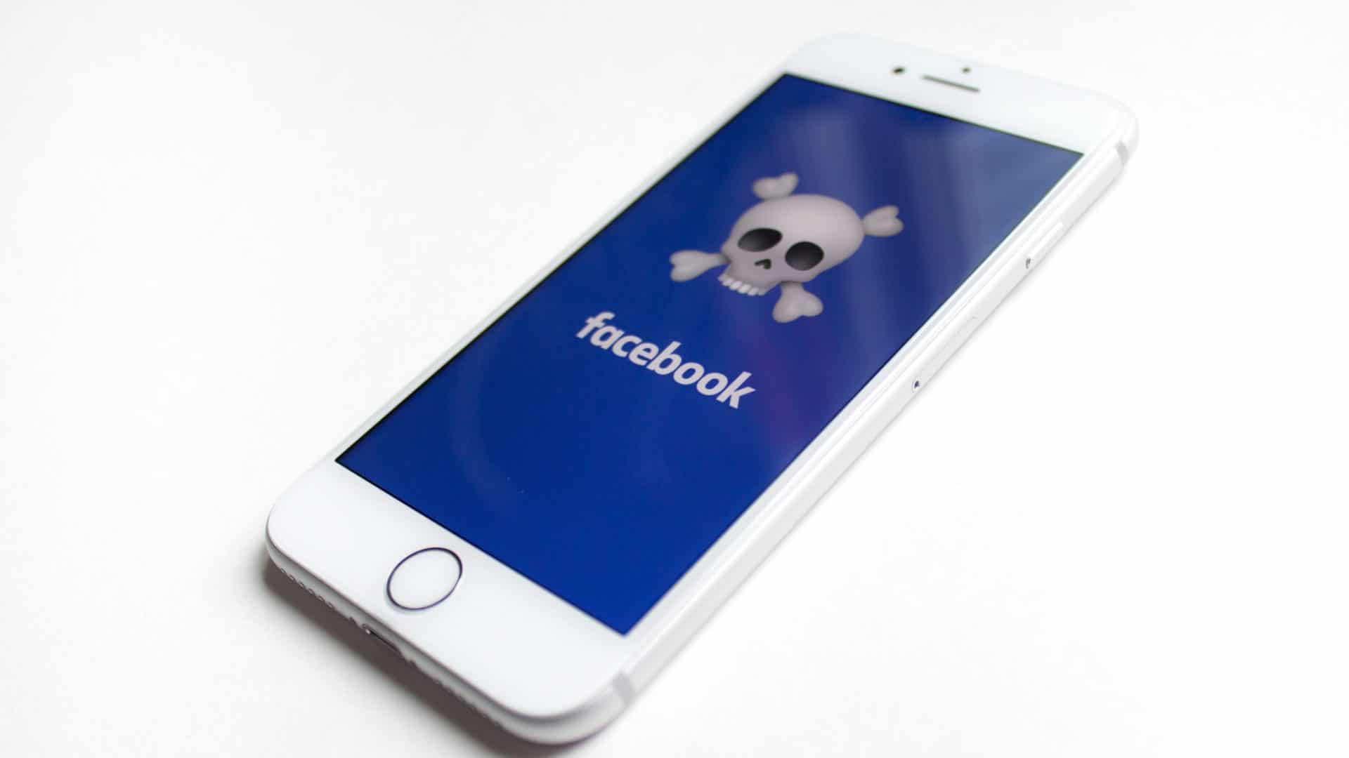 Aparelho celular com a tela inicial do facebook mas com um símbolo de caveira no lugar do logo