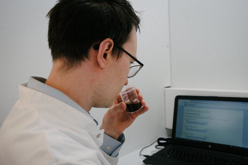 Imagem mostra um técnico de laboratório testando o sabor do café sustentável, com um notebook à sua frente