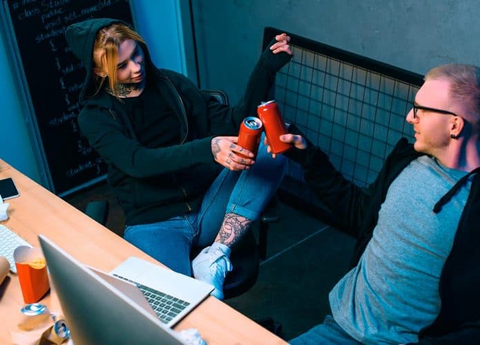 hackers brindando com duas latas de cerveja na frente de computadores