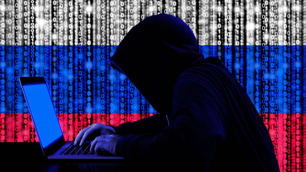 hacker de capuz digitando em teclado com letras sobrepondo ele e formando a bandeira da rússia