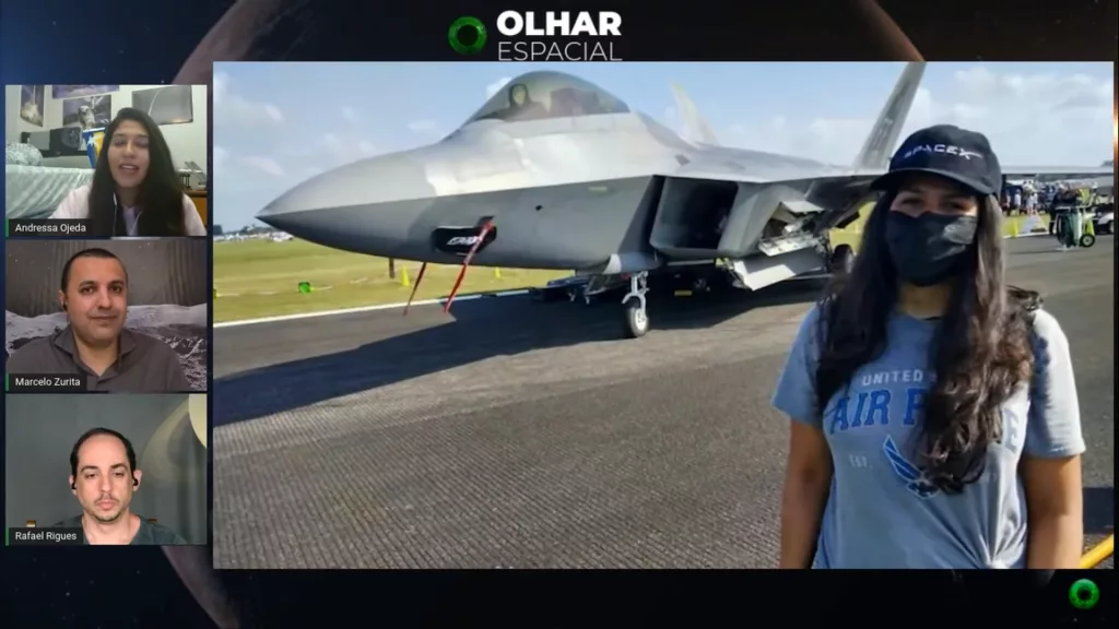 Imagem mostra Andressa Ojeda, Marcelo Zurita e Rafael Rigues em uma coluna à esquerda, em uma videoconferência que compartilha imagens de Andressa à frente de um avião de caça da Força Aérea americana. Andressa veste um boné da SpaceX, e seus cabelos longos cobrem o logotipo da força aérea. No rosto, ela usa uma máscara preta de proteção